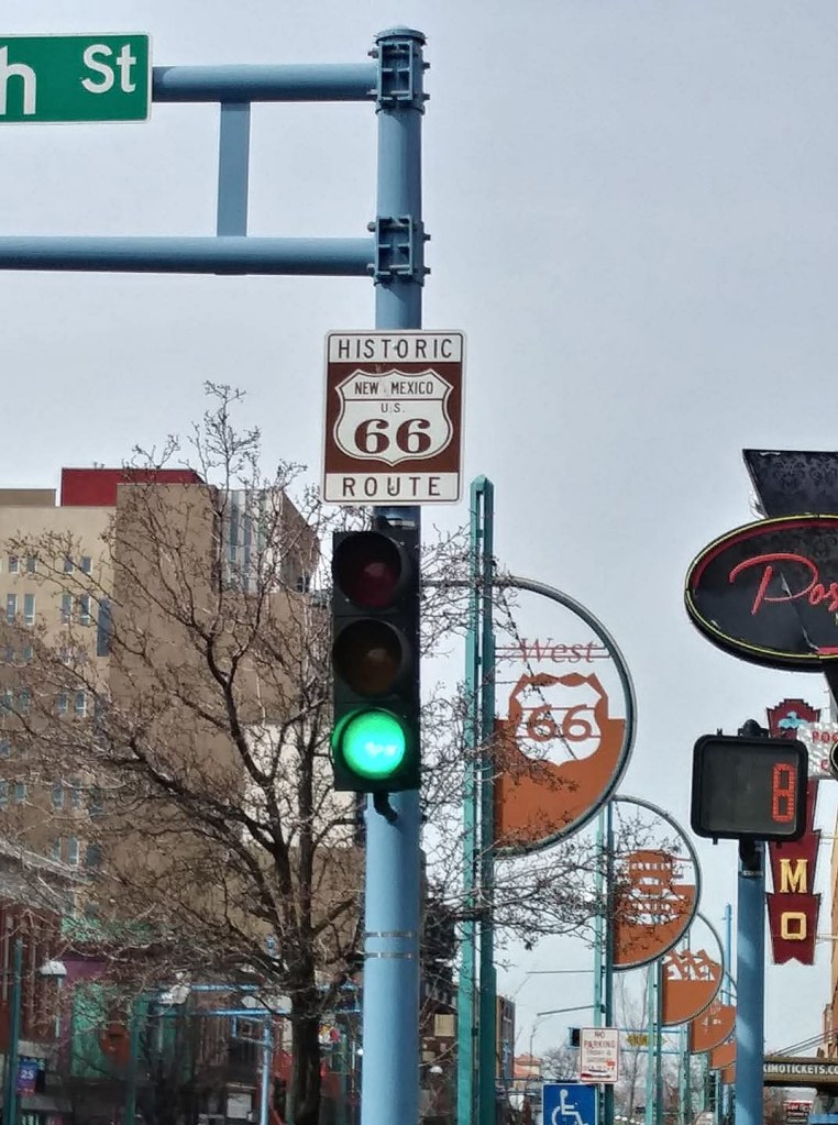 Traffic light displaying green with a historic Route 66 sign underneath and street signage in the background.