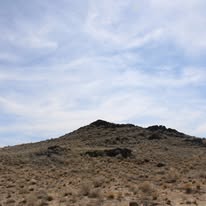 A rocky hill in a dry, desert landscape under a cloudy sky.
